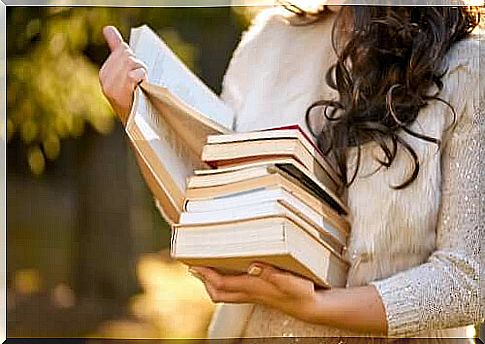 A woman carries a stack of books